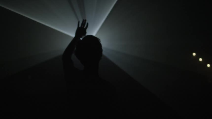A young man holding up his arm and walking towards a strobe light