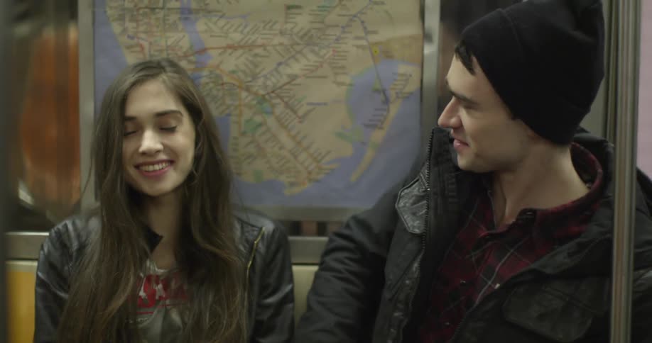 A man smiles as a woman sits next to him on the subway, and they start to talk and laugh