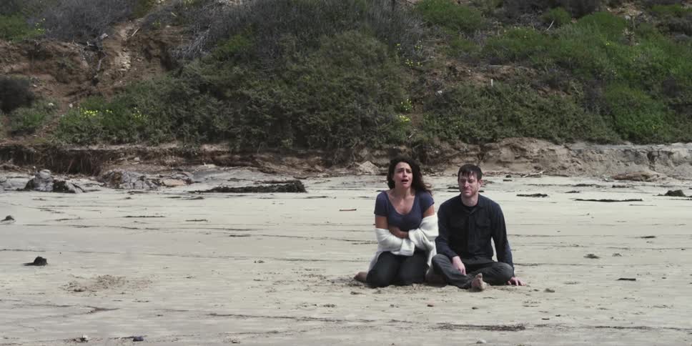 A woman panics on a beach with a man sitting next to her