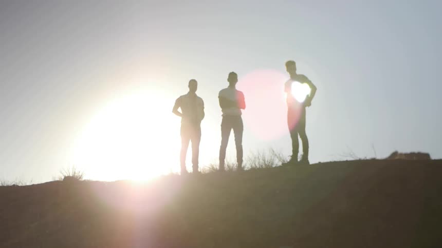Three men standing around at the top of the hill with the sun glaring brightly behind them