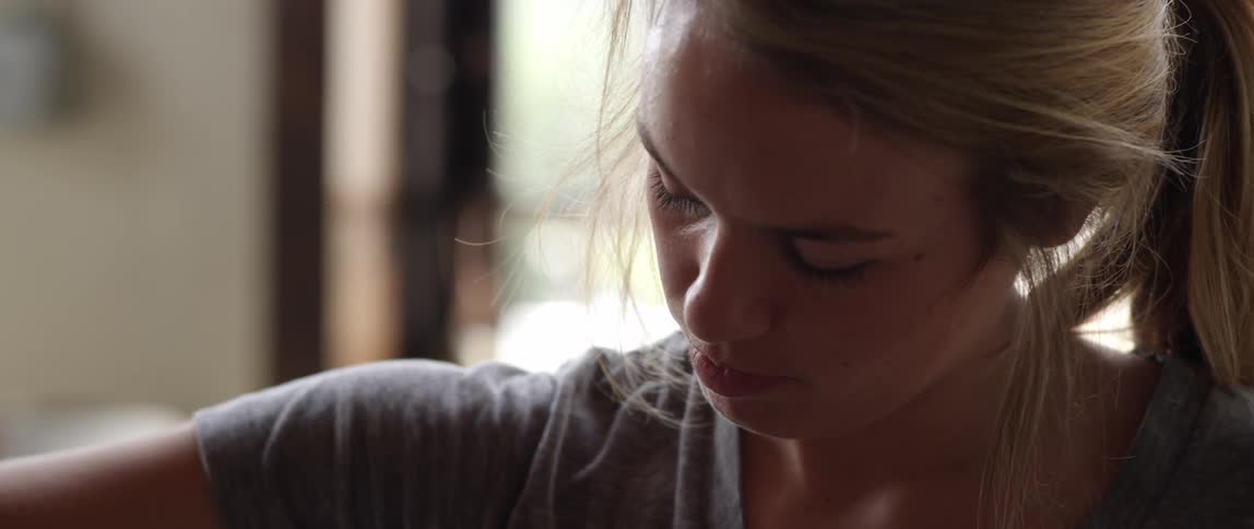 A blonde woman looking down at something and then picking up an unfolded coffee cup sleeve