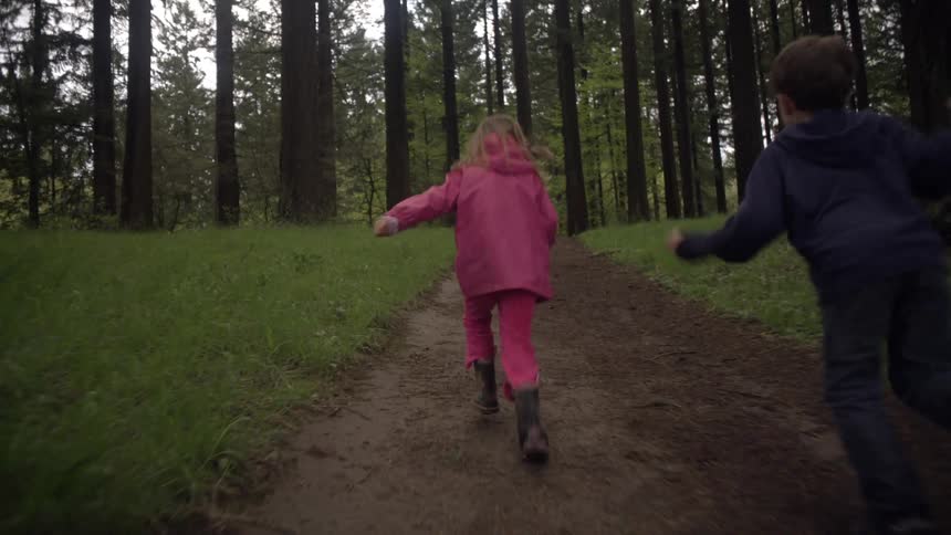 Three children run down a dirt path in the woods
