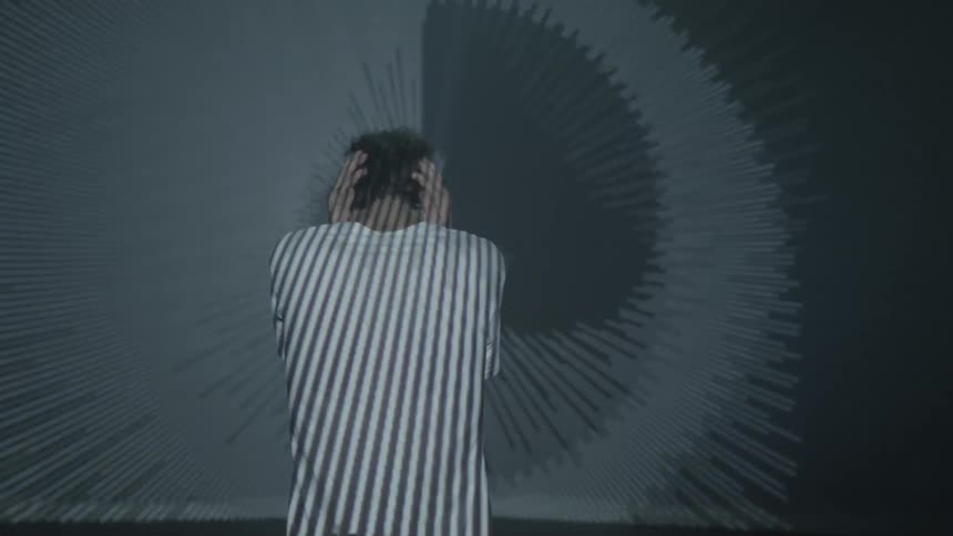 A man holds his ears while lights make different patterns around and on him